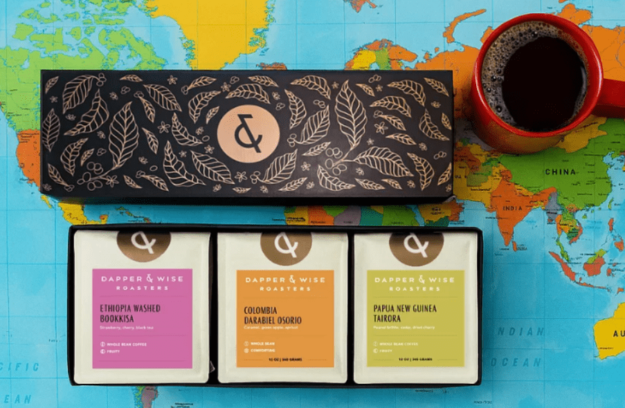 Specialty coffee gift set with labeled boxes placed on a colorful world map beside a cup of coffee.